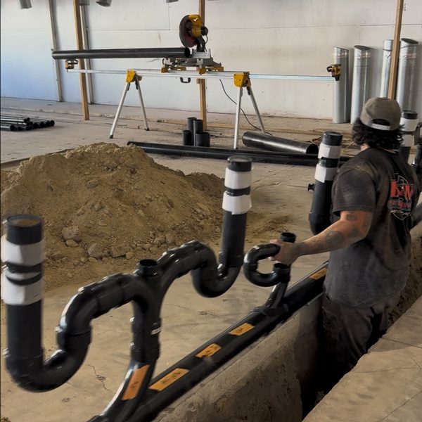 A plumber fitting new black drain lines into the trench at Spinwave Laundry